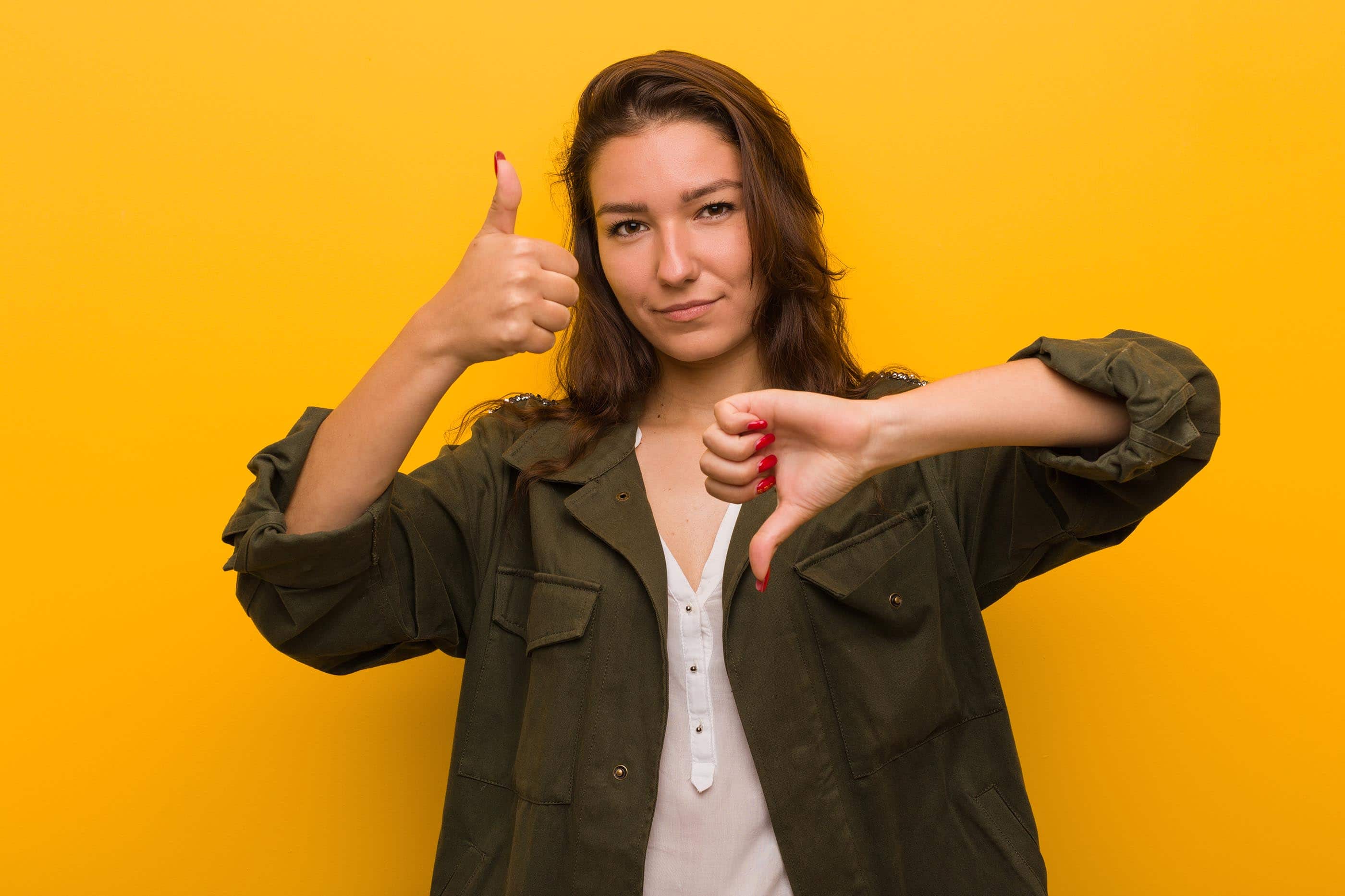 Young woman isolated over yellow background showing thumbs up and thumbs down.