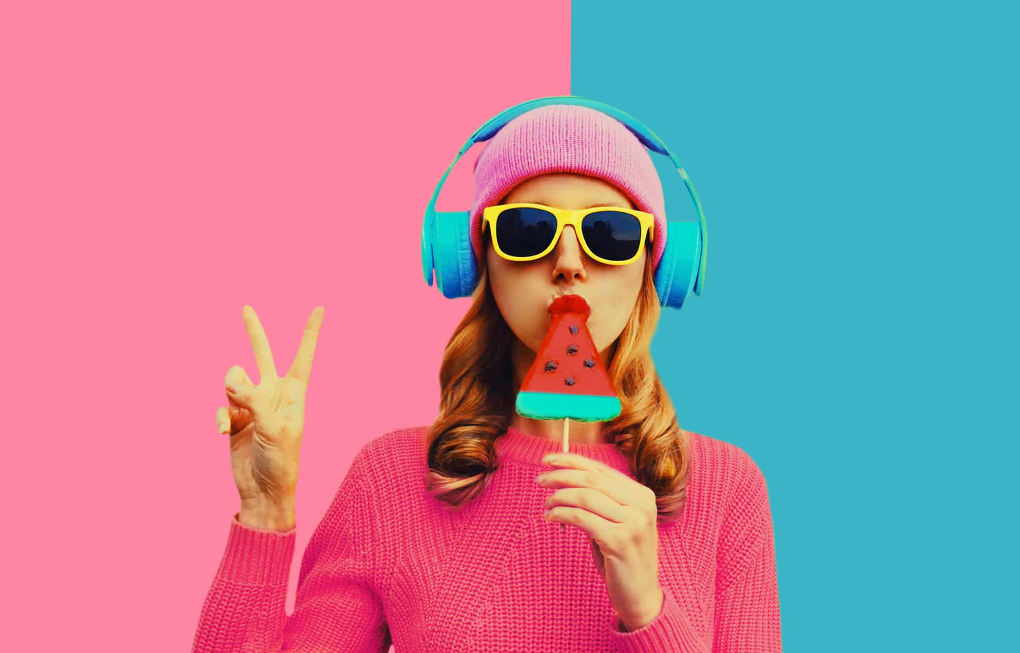 Summer portrait of stylish cool young woman in headphones listening to music with fruit juicy lollipop or ice cream on colorful background