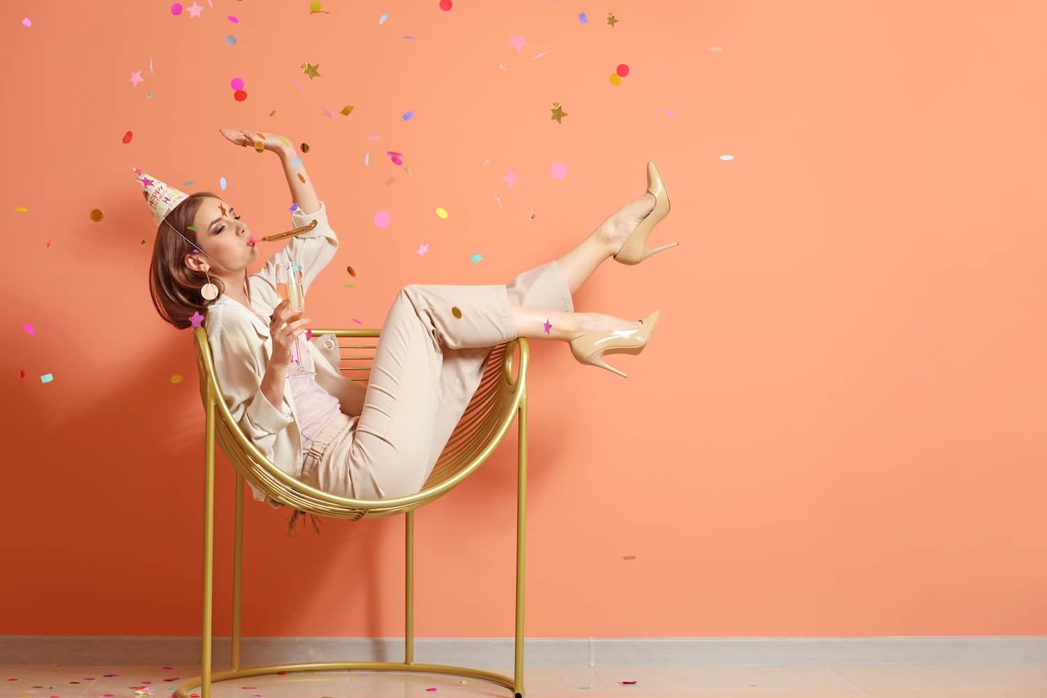 Happy woman with party whistle and glass of champagne near color wall